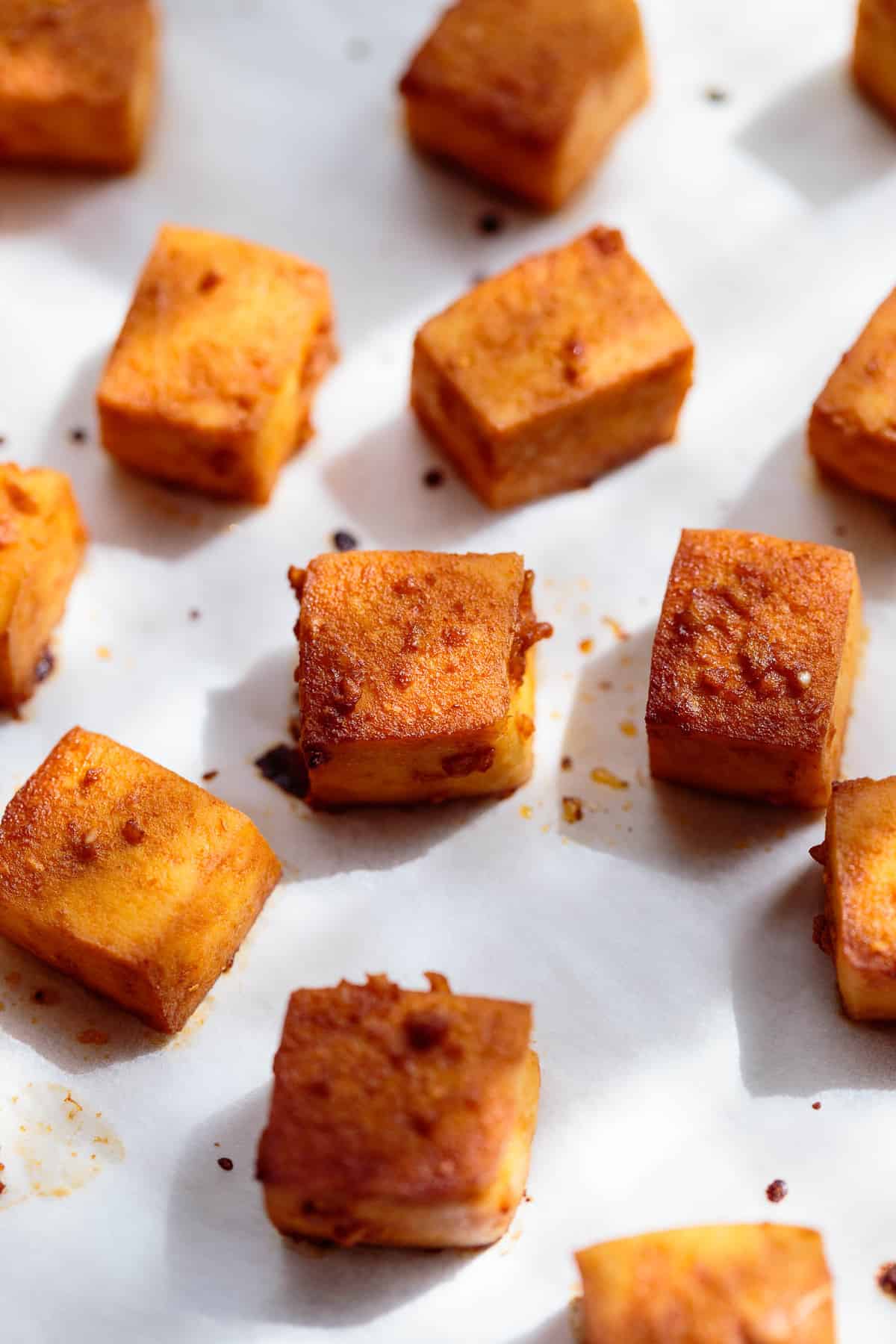 Baked marinated tofu cubes on parchment paper.