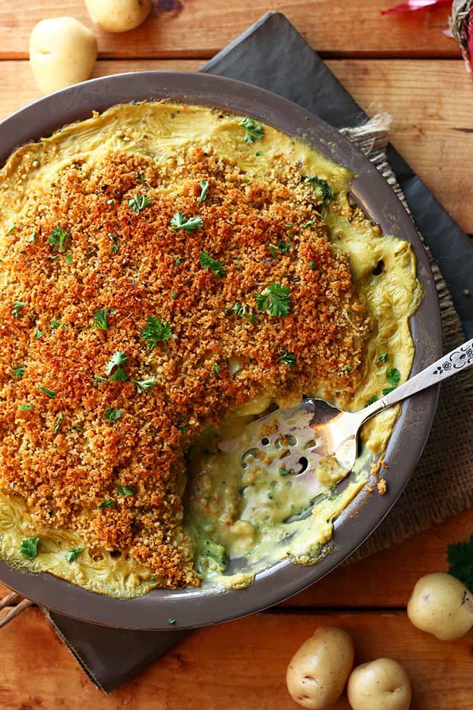 Close up of baked Cheesy Vegan Potato & Broccoli Casserole with a serving spoon and one portion already served.
