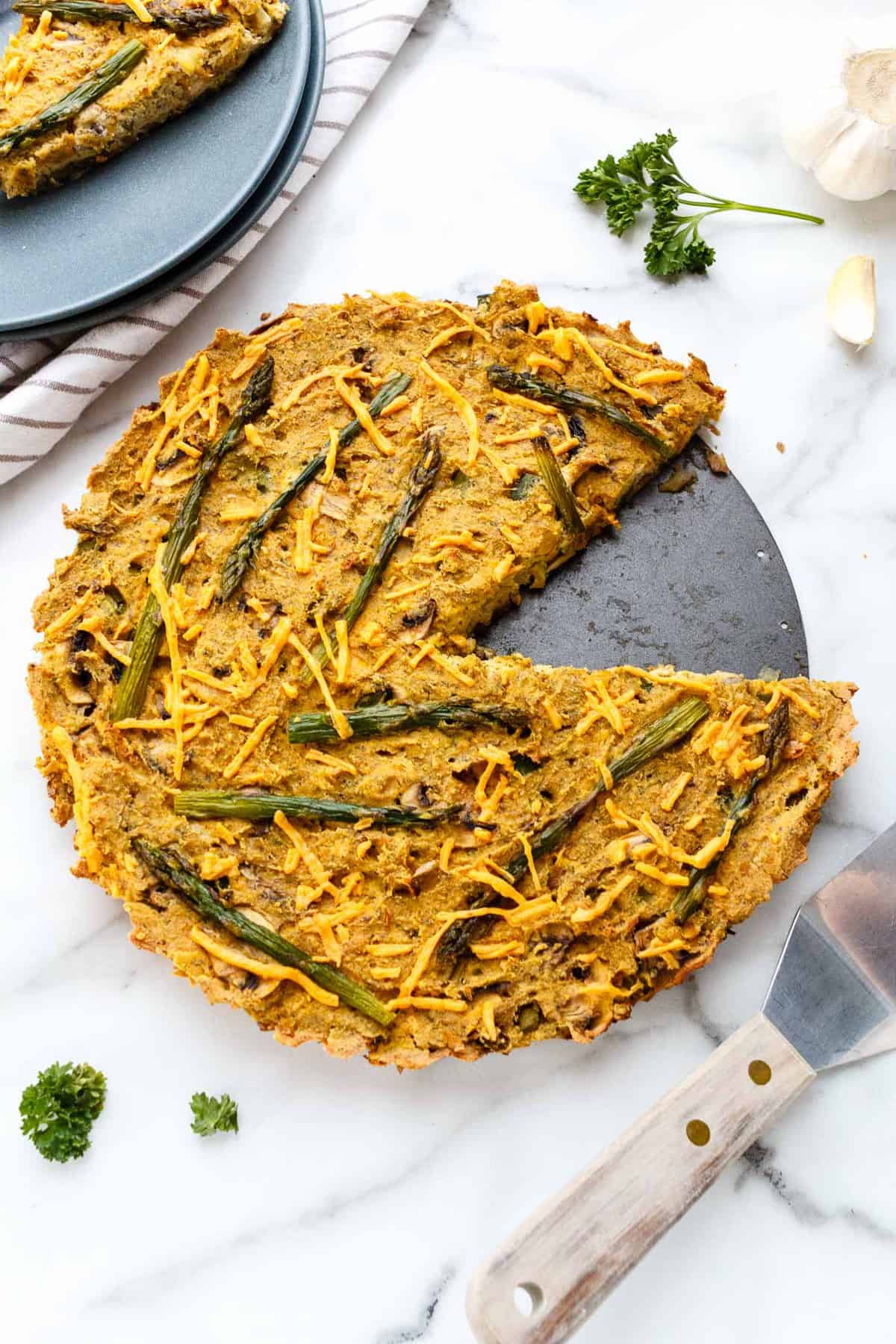 Vegan asparagus and mushroom quiche with hash brown crust with one piece cut out.