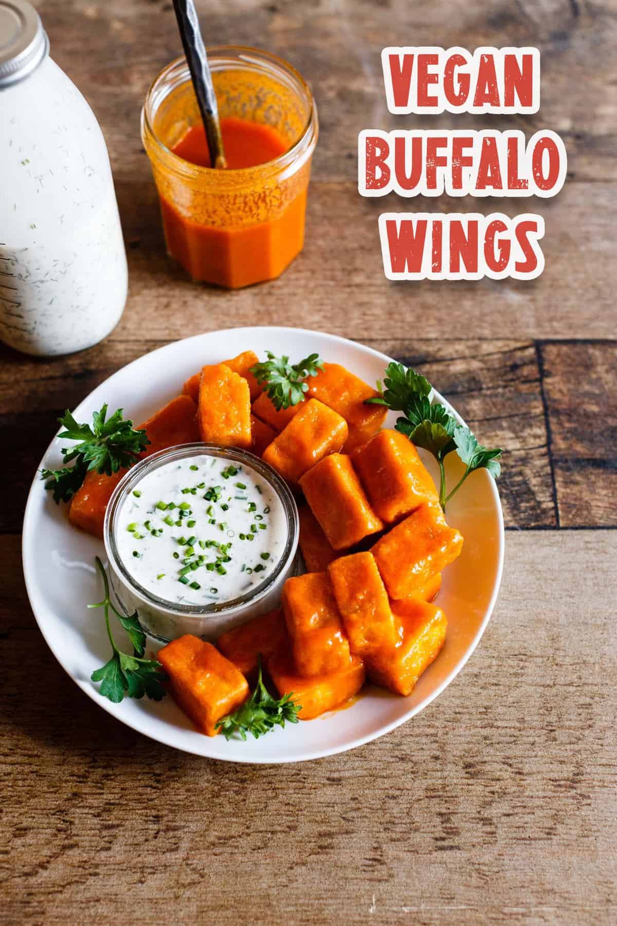 Overhead view of Vegan Spicy Buffalo Tofu "Wings" with homemade Vegan Ranch Dressing on a dark wood background and text overlay reading "Vegan Buffalo Wings"