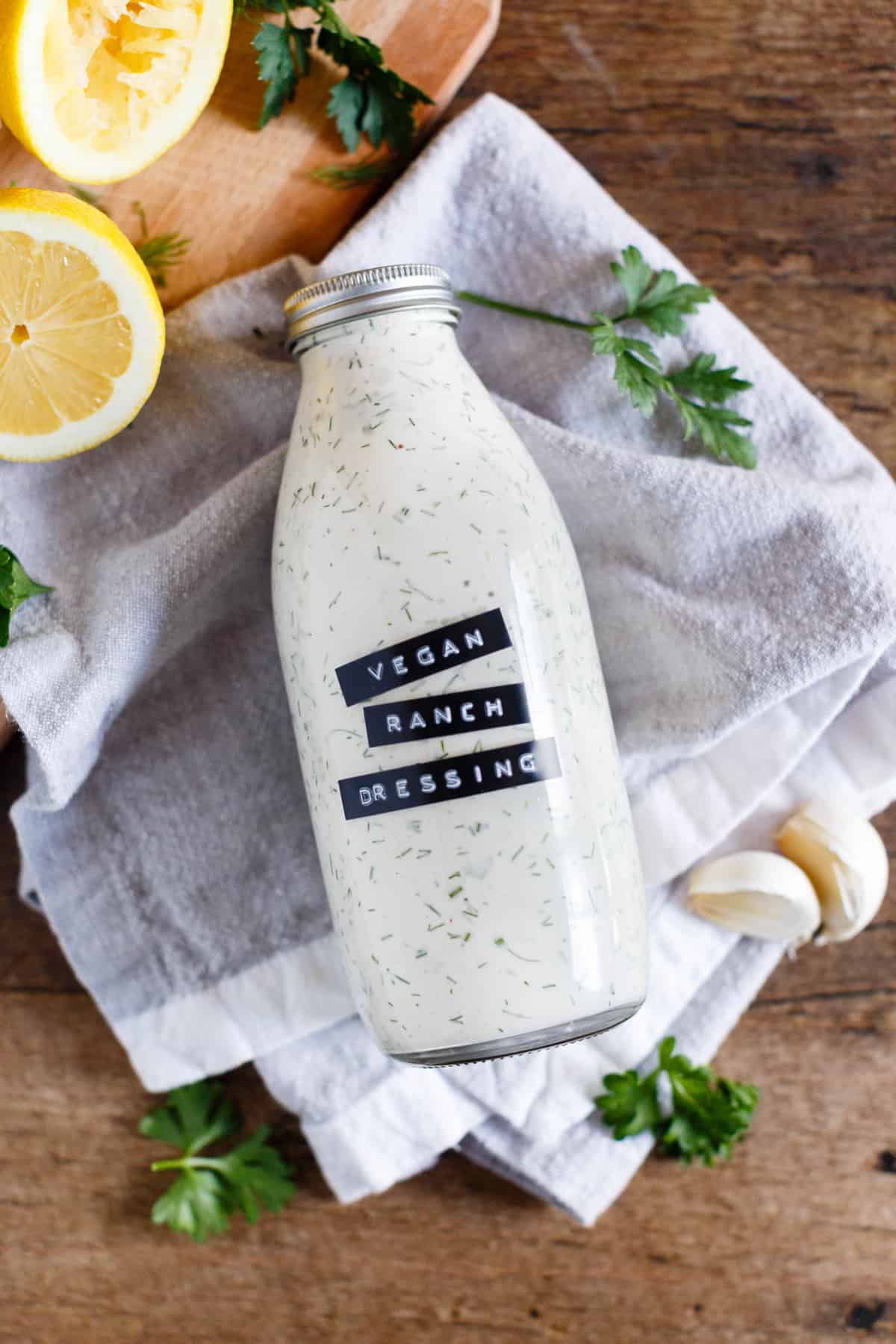 Bottle of homemade vegan ranch dressing laying on a grey kitchen towel.