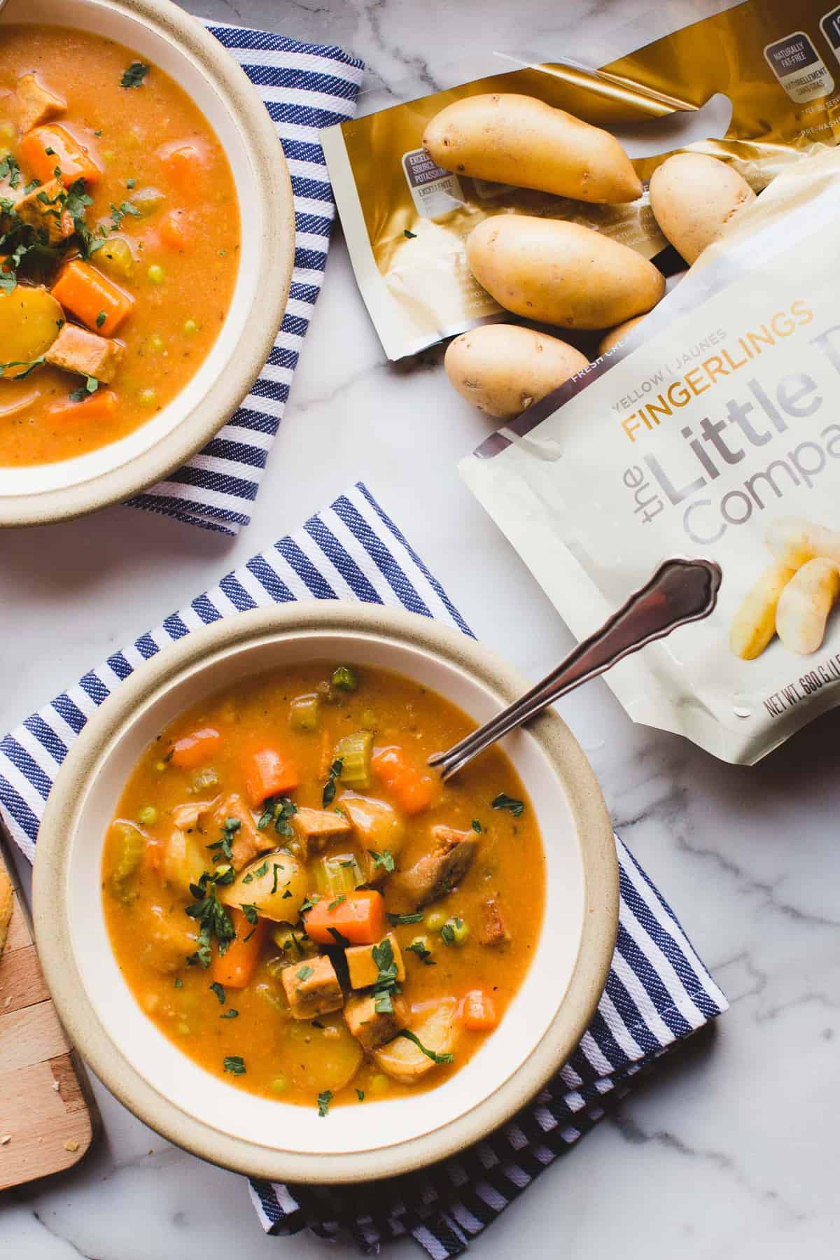 Two bowls of Instant Pot Vegan Tofu & Little Potato Stew served with French bread on a marble countertop.