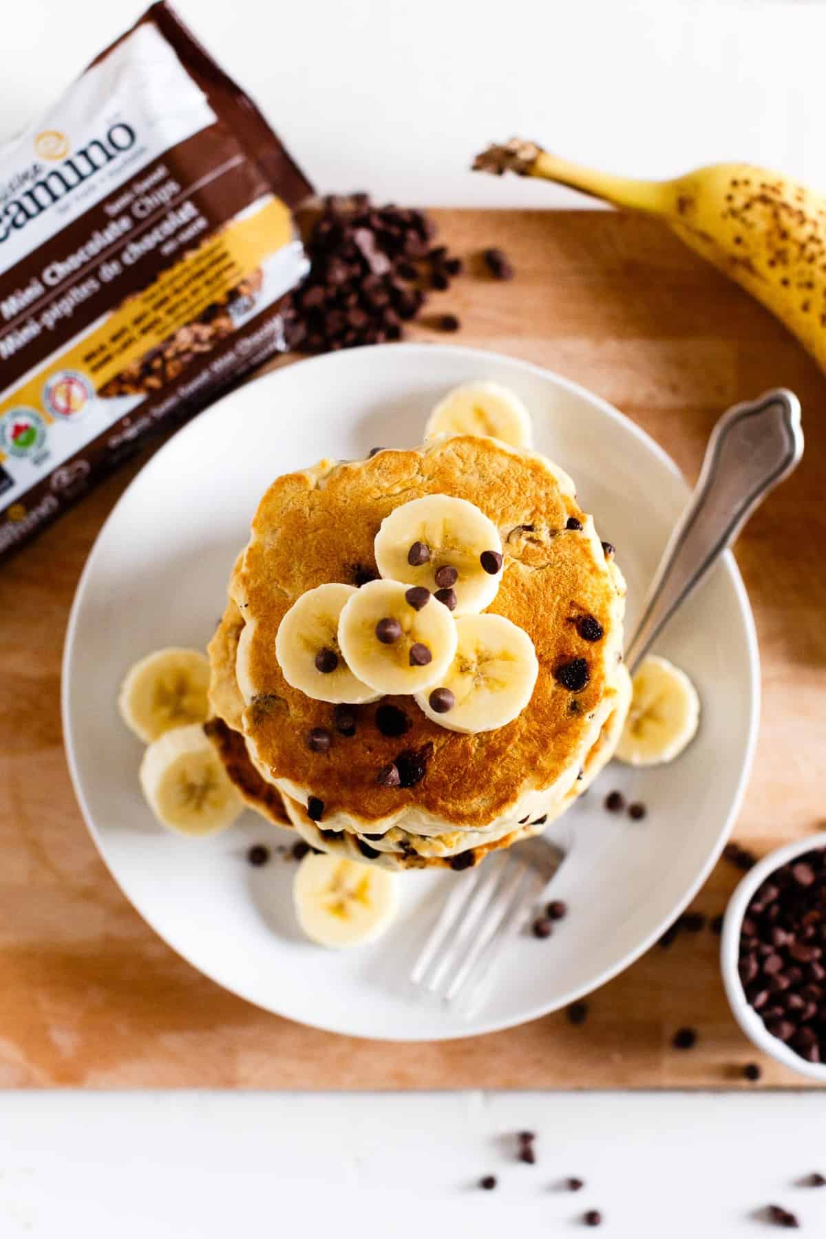 Overhead view of a stack of vegan chocolate chip pancakes topped with sliced banana and chocolate chips.