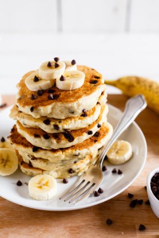 Stack of vegan chocolate chip pancakes topped with sliced bananas.
