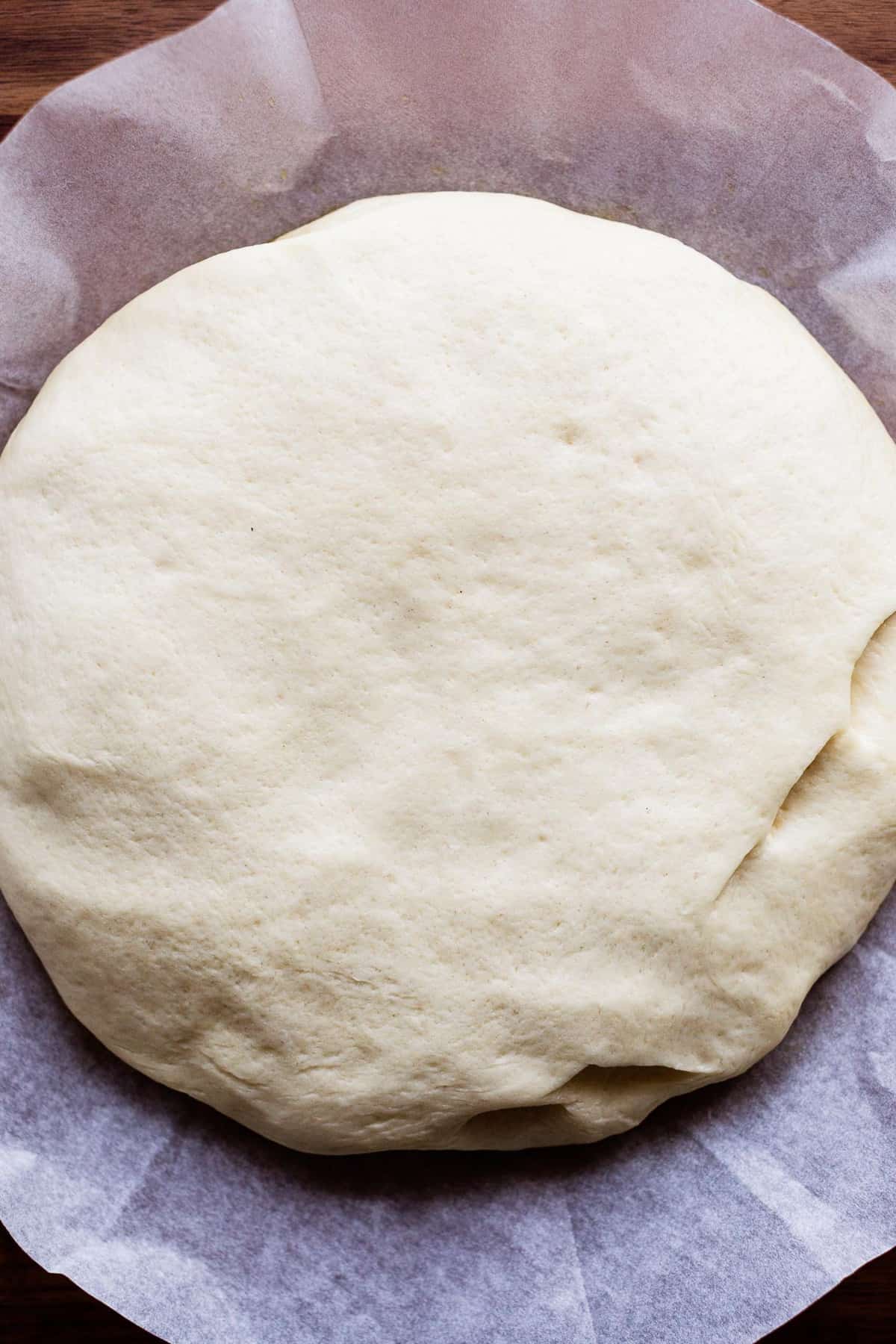 Risen focaccia dough on parchment paper, ready to be dimpled.
