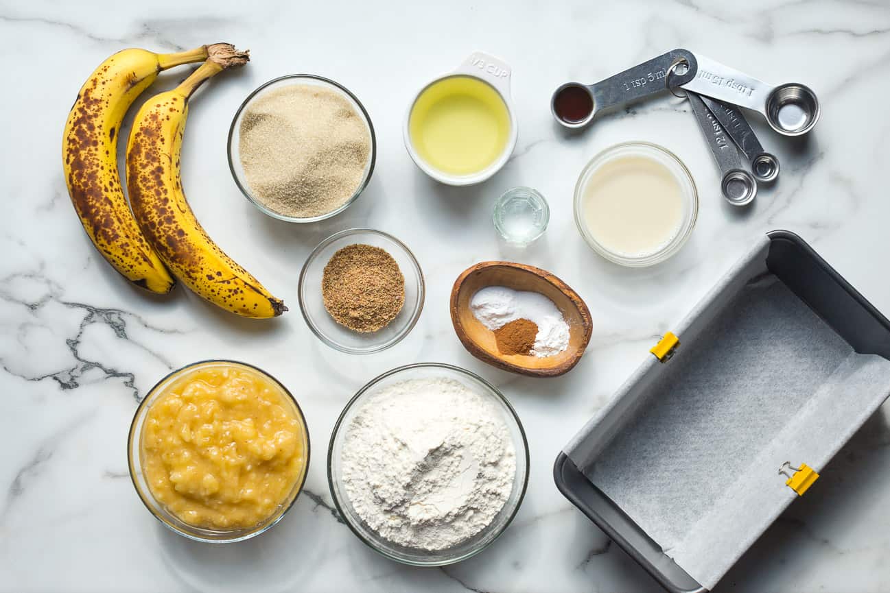 Prepared and measured ingredients for making vegan banana bread on a marble counter top.