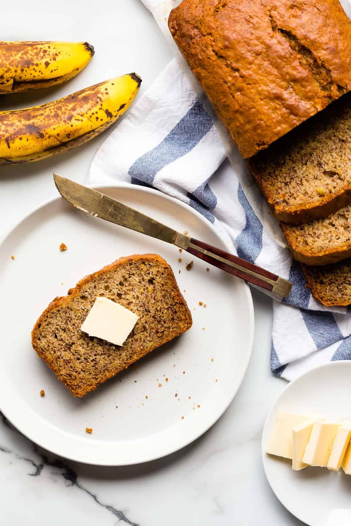 A slice a vegan banana bread on a plate with a pat of vegan butter.