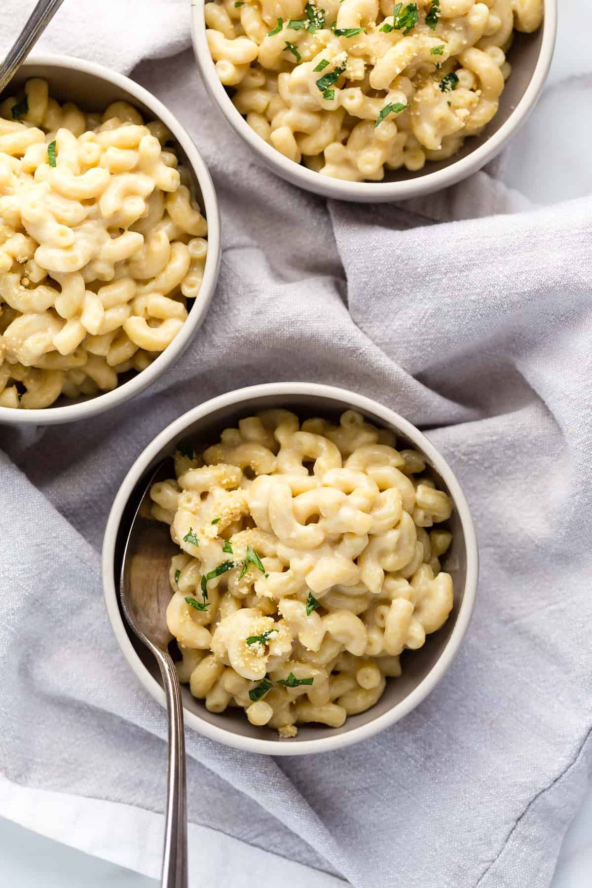 3 small bowls of vegan mac and cheese topped with vegan cashew parmesan and chopped parsley.