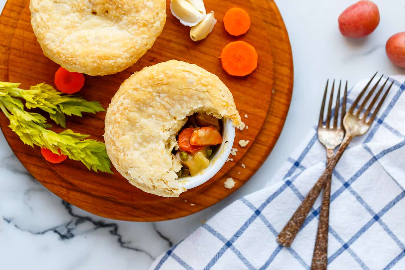 Vegan pot pies topped with flaky pastry crust on a round teak cutting board.