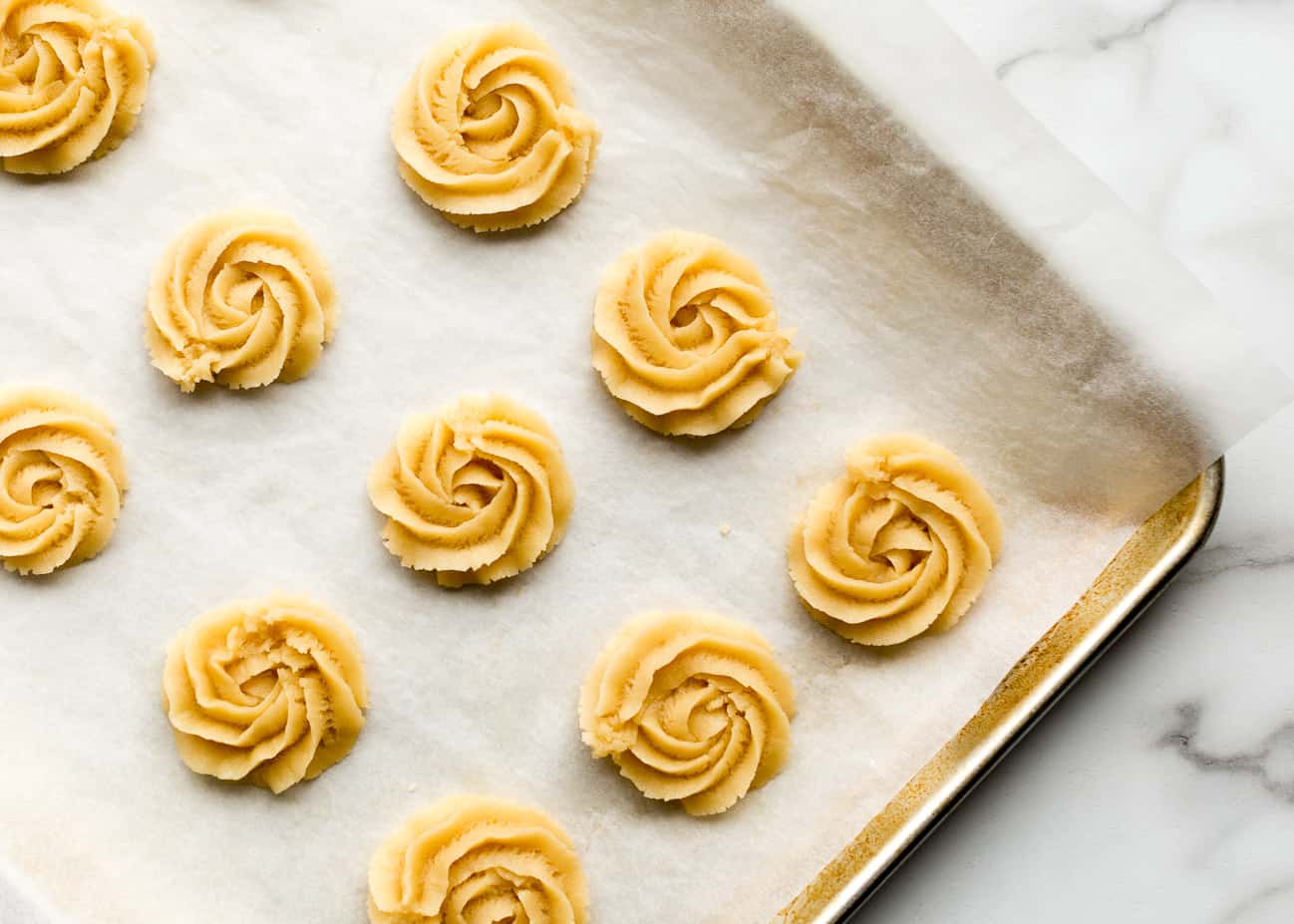 Unbaked, piped vegan butter cookie swirls on a cookie sheet.