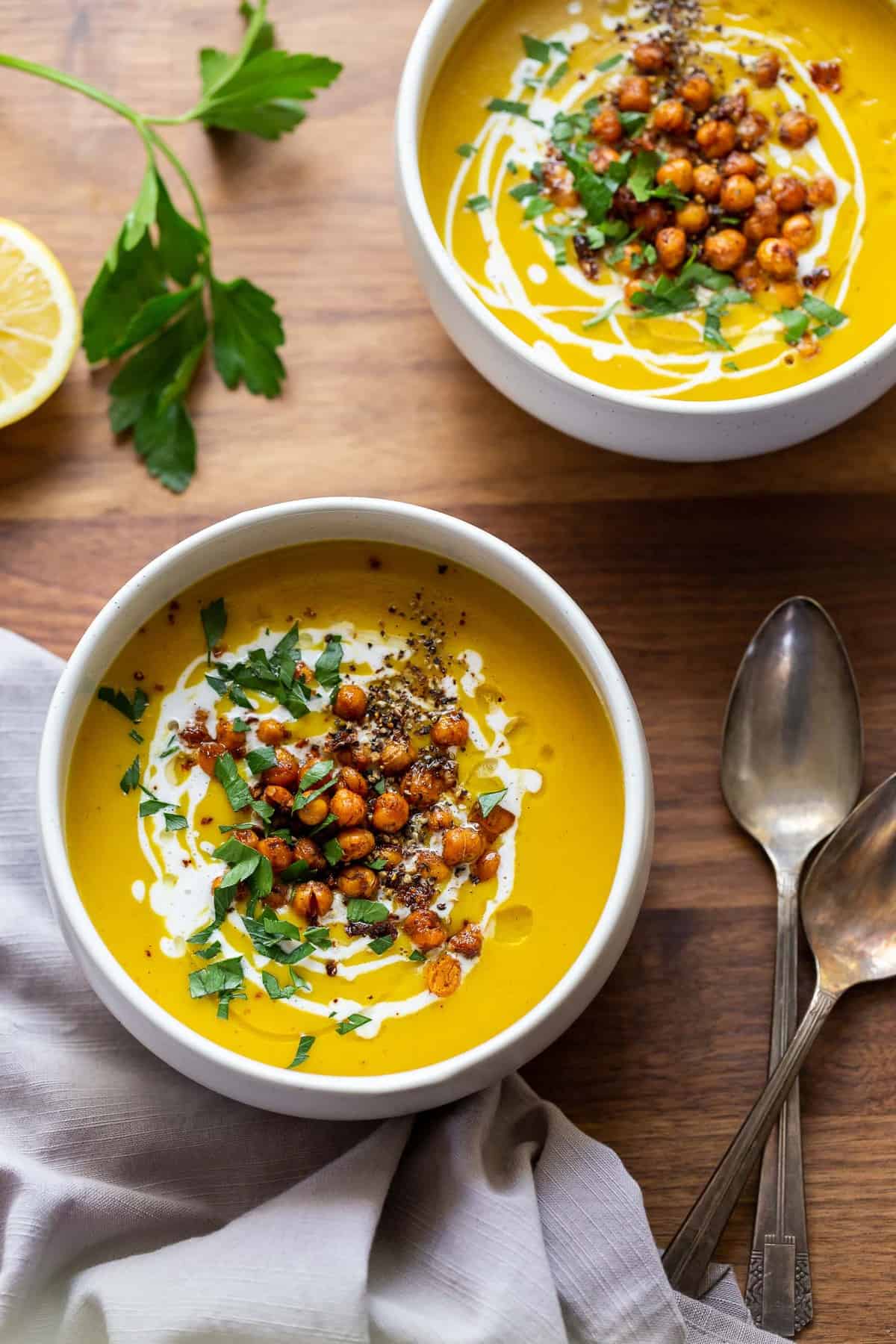 Two bowls of chickpea turmeric soup topped with a swirl of coconut cream, crispy spiced chickpeas, and chopped herbs.