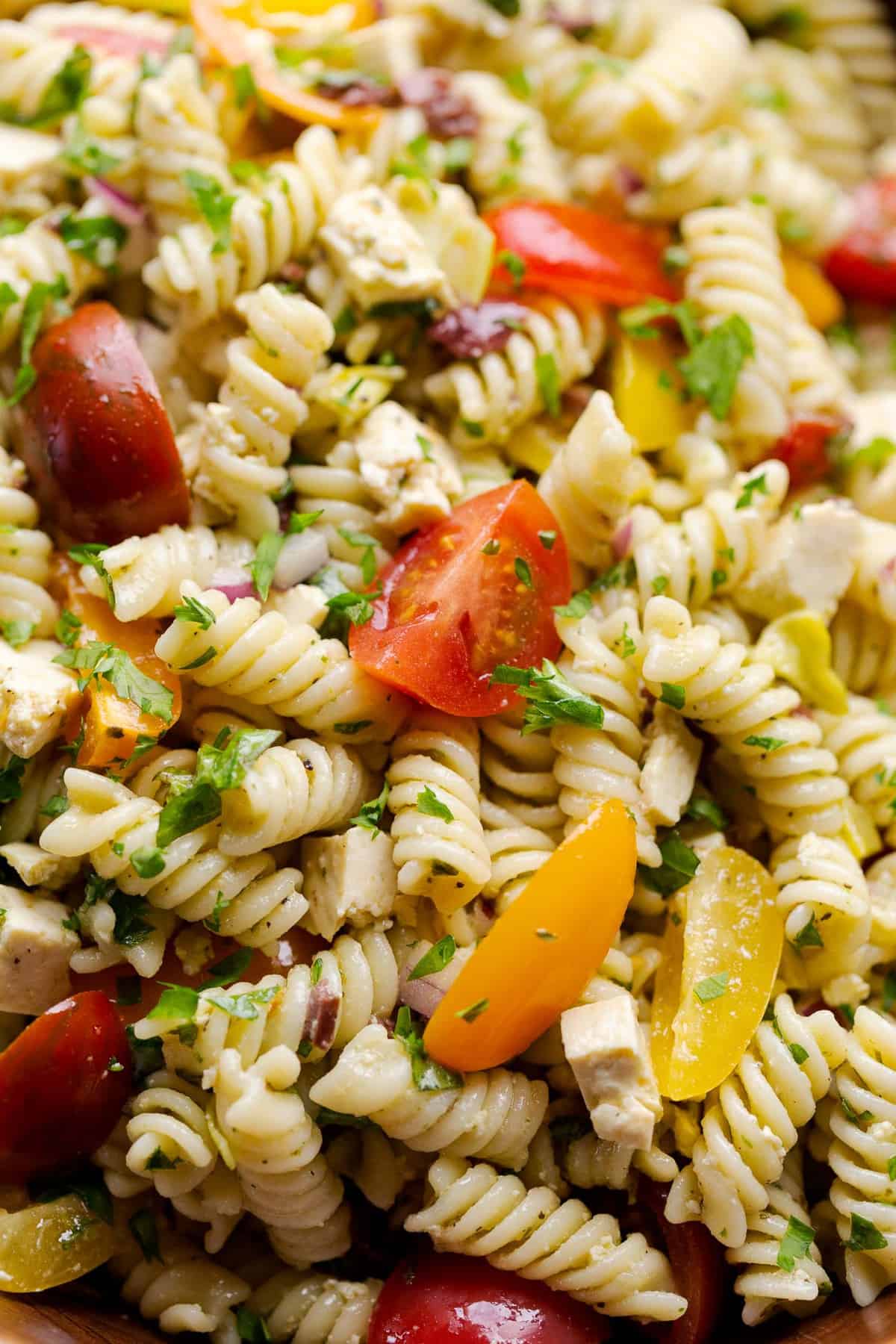 Close up of fusilli pasta, tomatoes, and herbs in vegan Italian pasta salad.