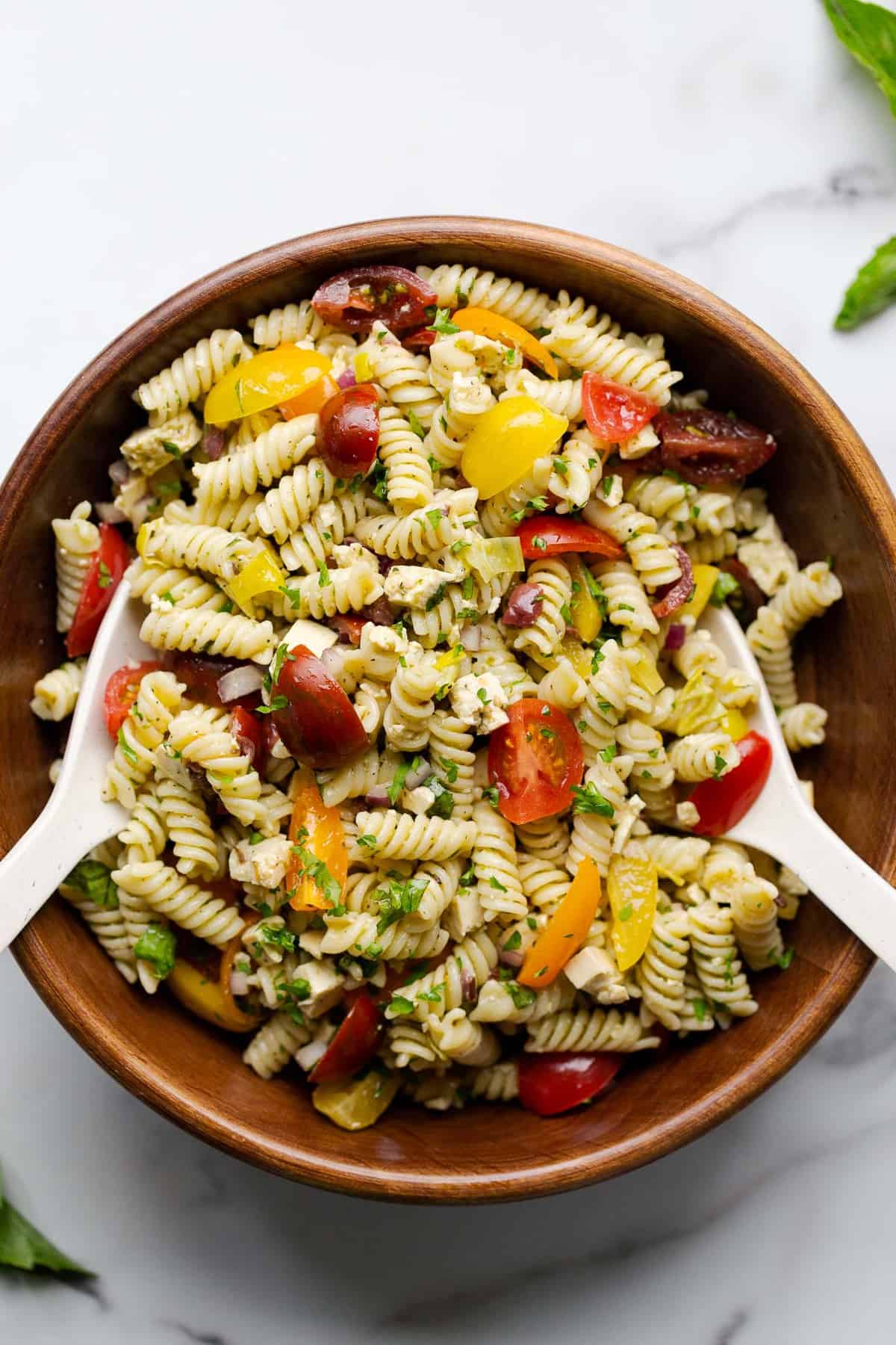 Vegan Italian pasta salad in a dark wooden bowl with salad tossing spoons.