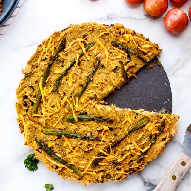 Vegan asparagus and mushroom quiche with hash brown crust with one piece cut out.