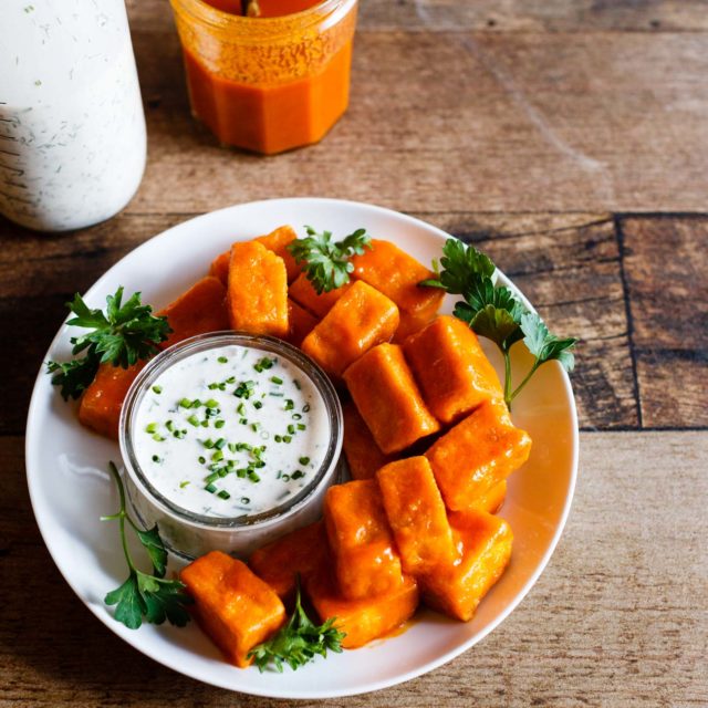 Overhead view of Vegan Spicy Buffalo Tofu "Wings" with homemade Vegan Ranch Dressing on a dark wood background.
