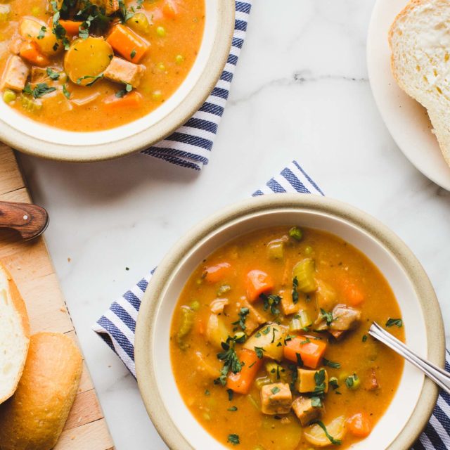Two bowls of Instant Pot Vegan Tofu & Potato Stew served with French bread on a marble countertop.