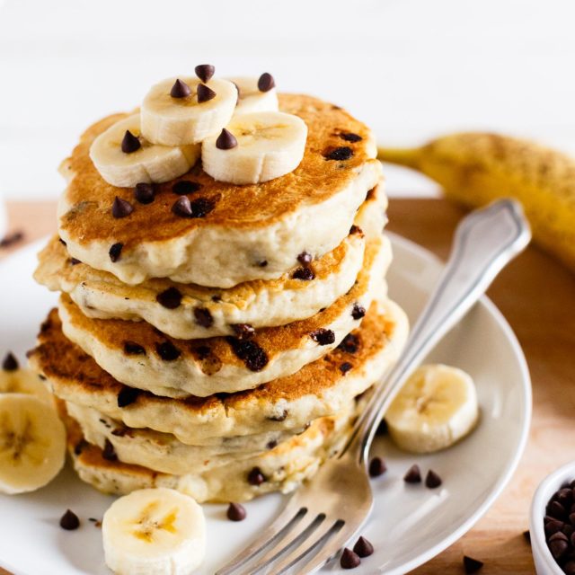 Stack of vegan chocolate chip pancakes topped with sliced bananas.