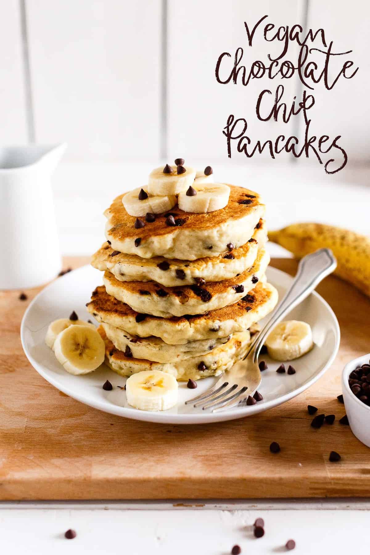 Stapel veganistische chocolate chip pancakes gegarneerd met plakjes banaan en maple syrup.