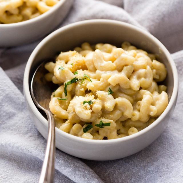 A small bowl of vegan mac and cheese topped with vegan cashew parmesan and chopped parsley.