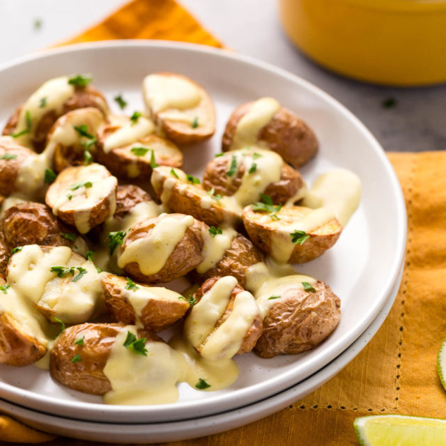 Roasted potatoes drizzled with vegan queso and sprinkled with fresh herbs.