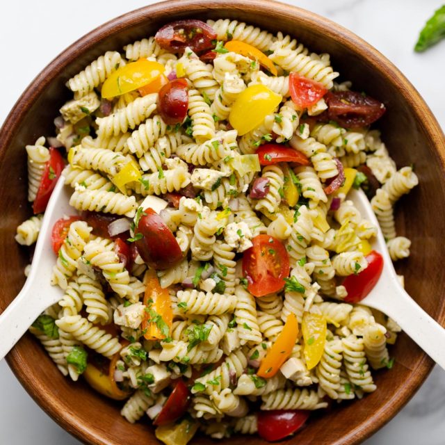 Vegan Italian pasta salad in a dark wooden bowl with salad tossing spoons.