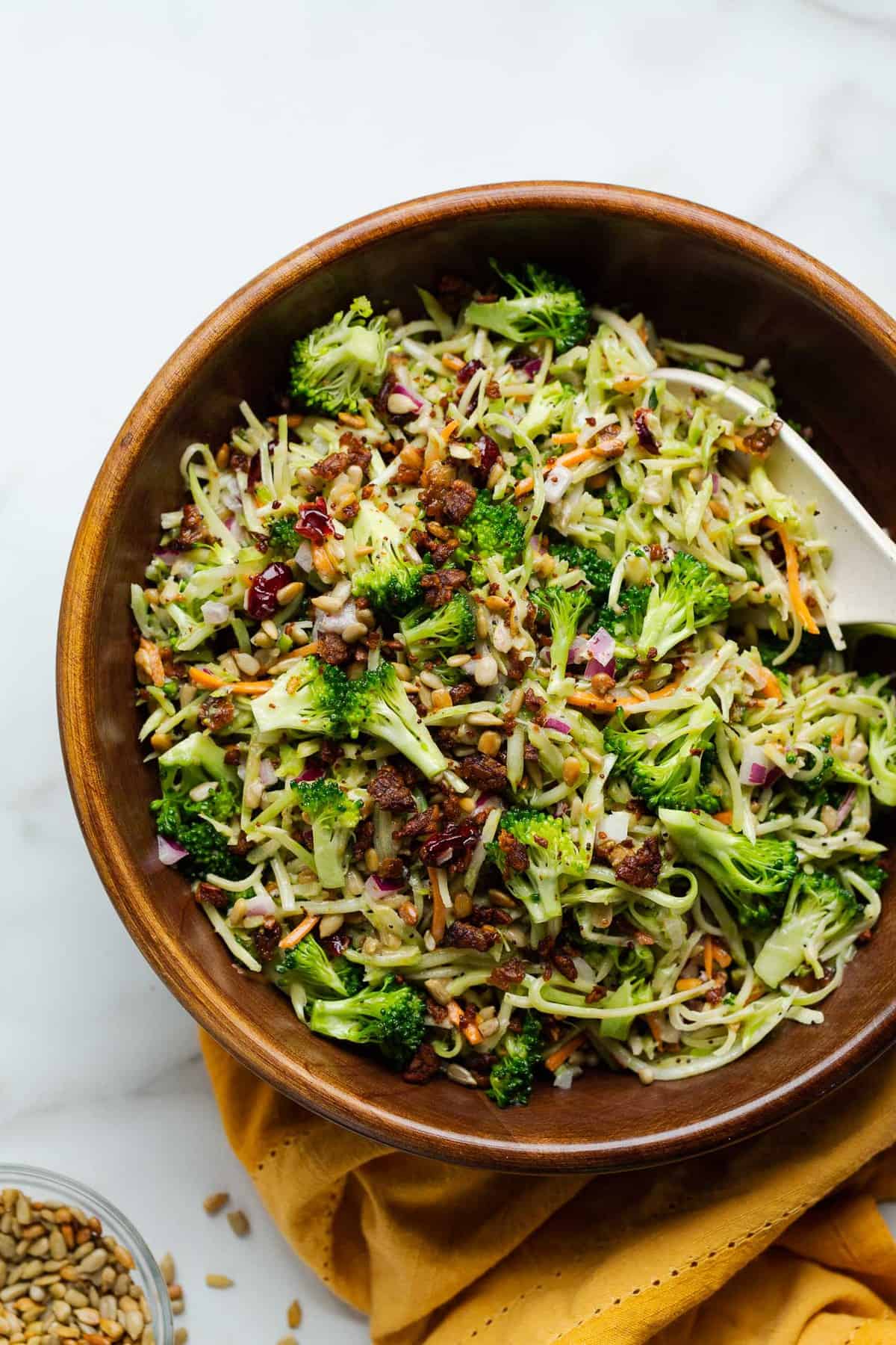 Vegan broccoli slaw salad and a serving spoon in a wooden serving bowl.