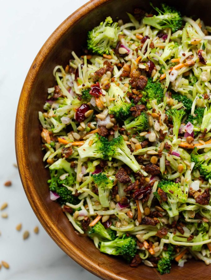 Vegan broccoli slaw salad in a wooden serving bowl sitting on a marble countertop.
