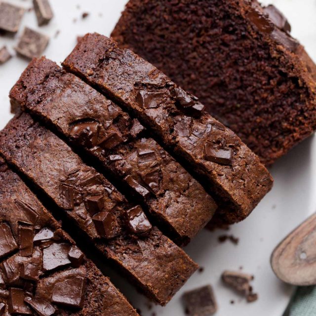 Close up, bird's eye view of a sliced loaf of vegan chocolate zucchini bread on a speckled white plate that showcases the chocolate chunks embedded into the top of the chocolatey loaf.